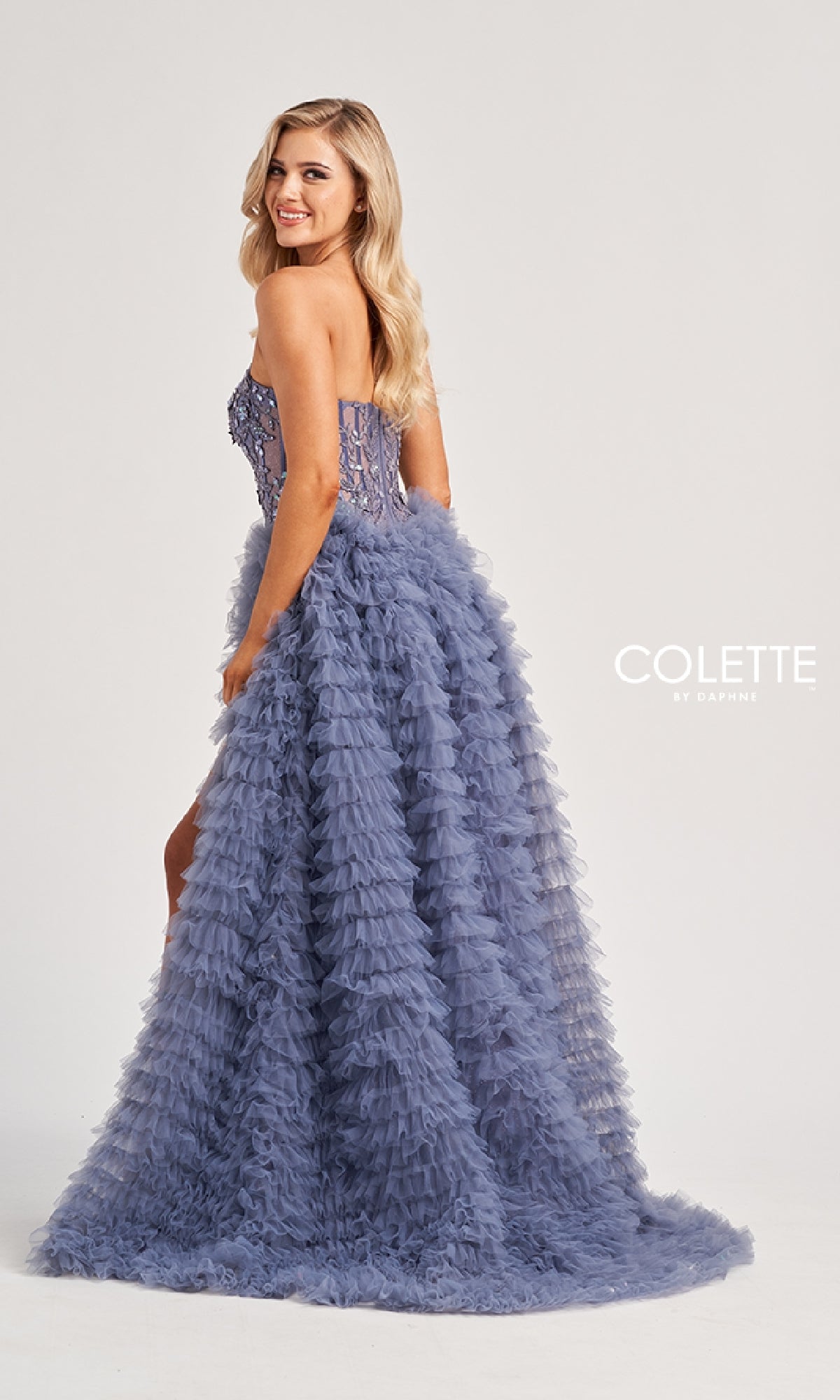 A woman poses in the Colette CL8170 long prom dress featuring a strapless, fitted bodice and layered tulle skirt in lavender. The